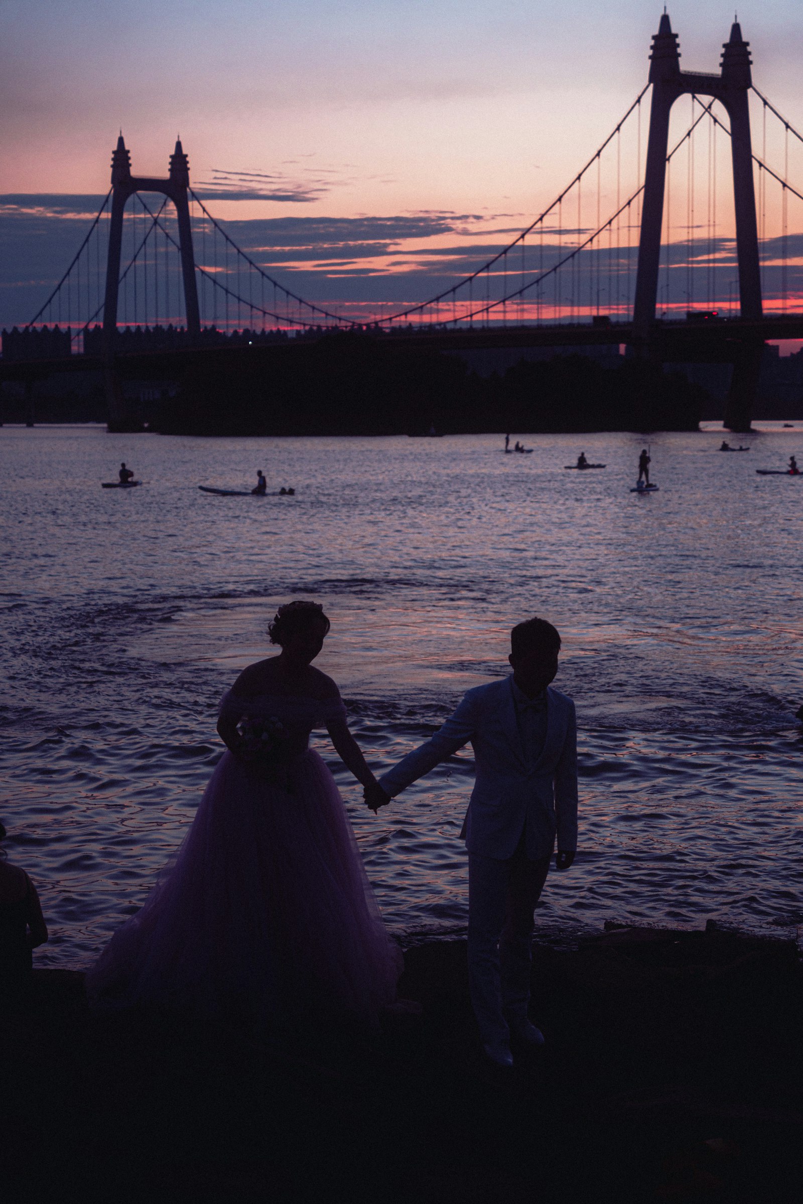 A couple holding hands by a bridge at sunset